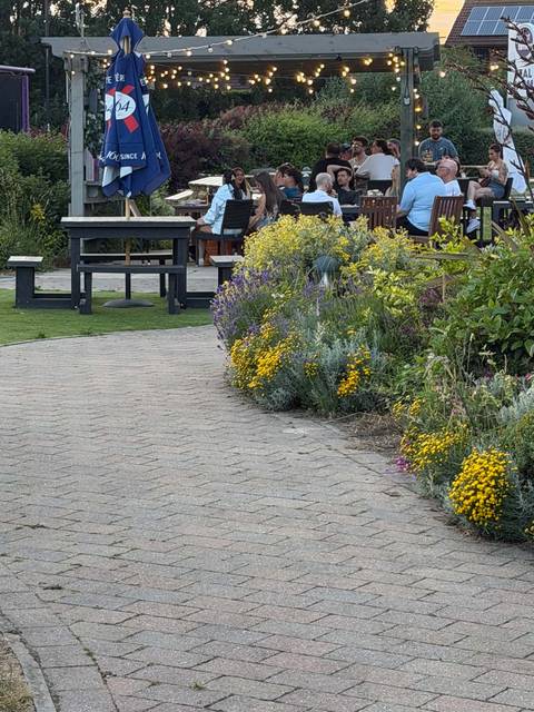The path through the Teal Farm garden on a busy evening, with flowers either side and people at the tables