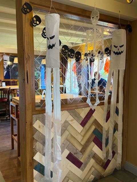 Halloween ghost decorations, a hanging skeleton and skull bunting on a wooden screen inside Teal Farm